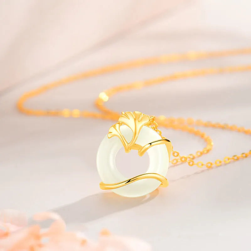 Close-up of a sterling silver peace buckle necklace with a cross chain and ginkgo details, shown in a gold tone.