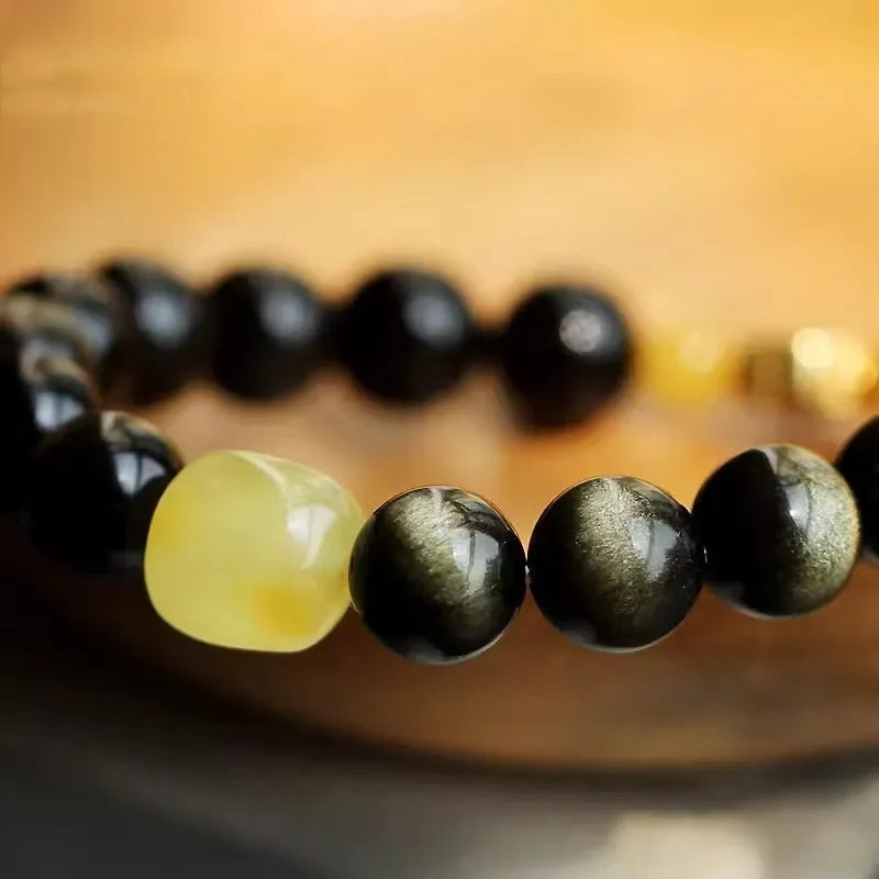 Handmade golden obsidian bracelet with geometric beads and zodiac charm on wrist.