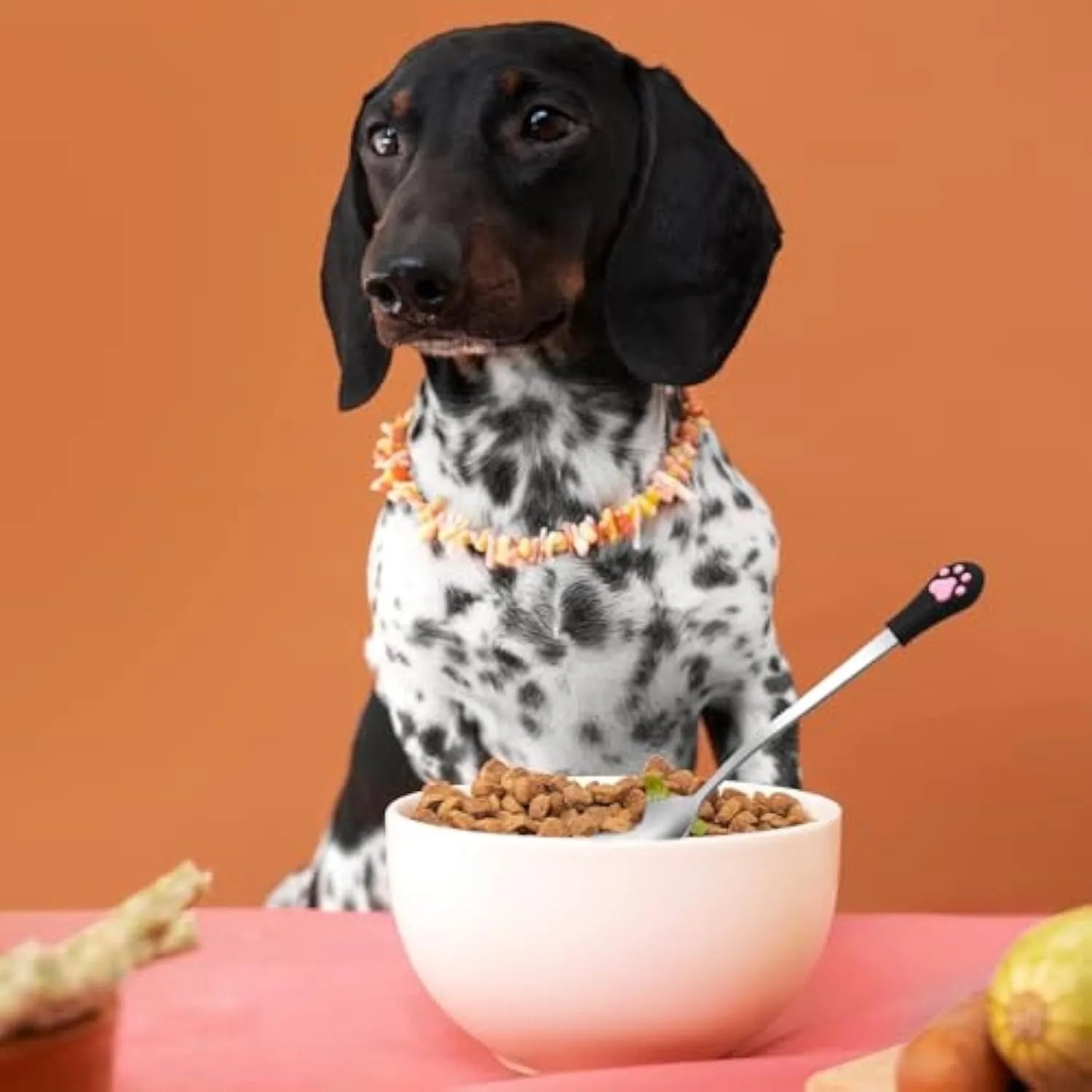 White and black stainless steel pet food spoons with silicone cat paw print handles on a table.