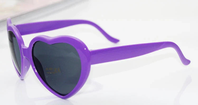 Heart-shaped glow-in-the-dark sunglasses in various vibrant colors, featuring a durable plastic frame and resin lenses for reliable UV protection.