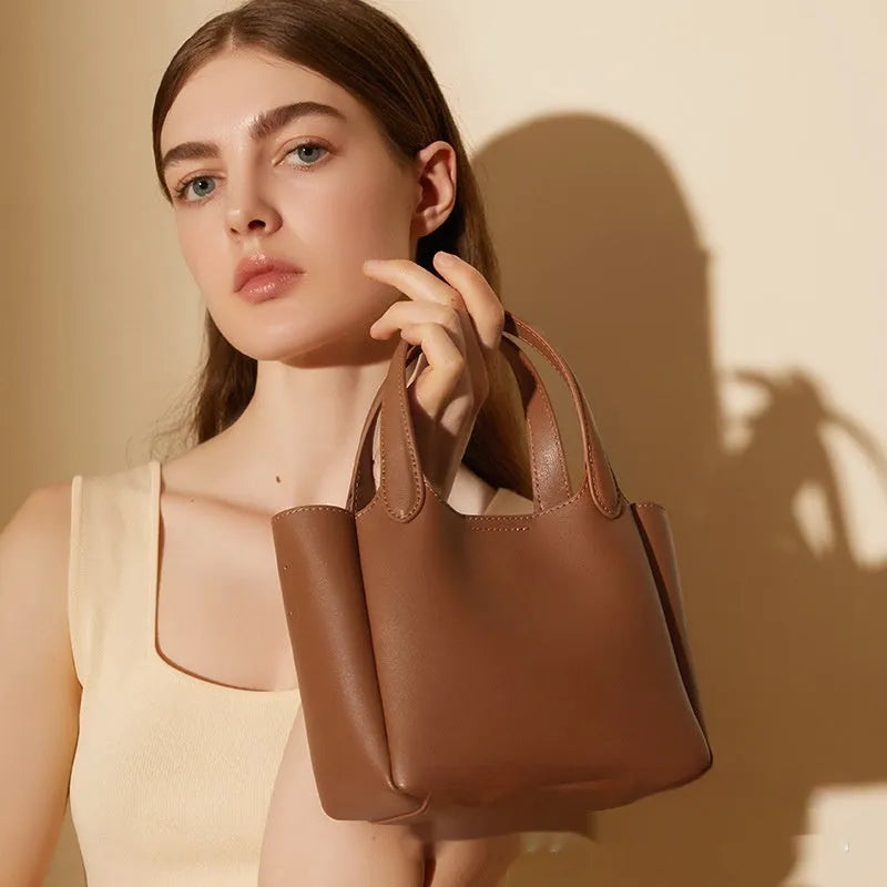 Brown cattlehide leather cross body bucket bag with square vertical shape and visible stitching