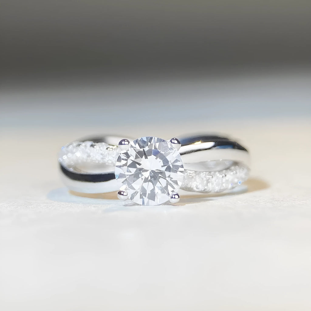Close-up of a silver geometric ring with a twisted band and a 1-karat moissanite stone in a four-claw setting.