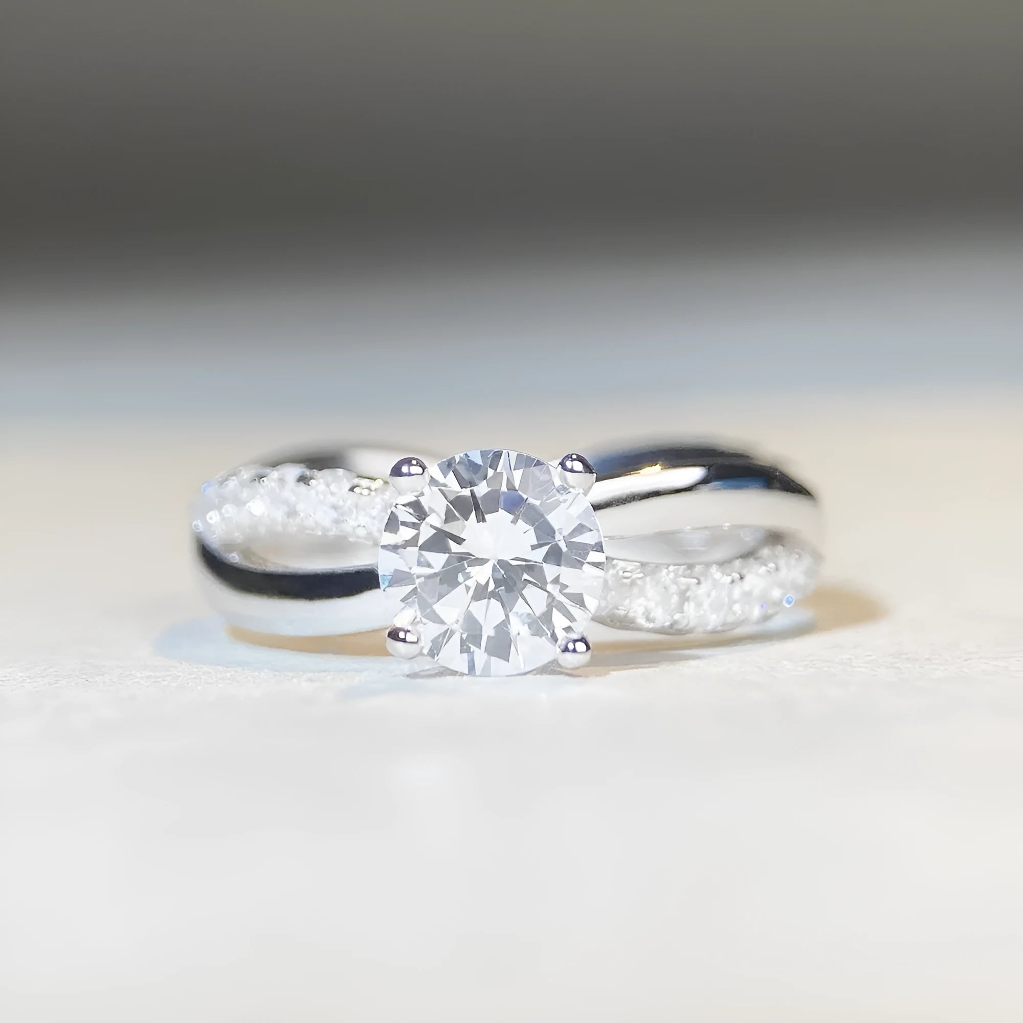 Close-up of a silver geometric ring with a twisted band and a 1-karat moissanite stone in a four-claw setting.
