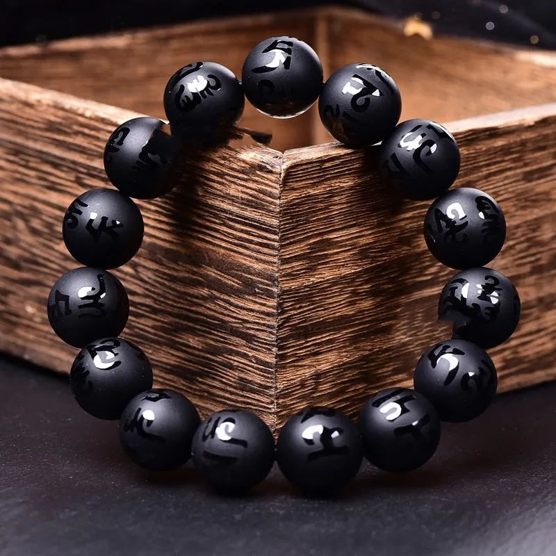 Close-up of a frosted black agate bracelet with an engraved Sanskrit mantra, showing stone texture.