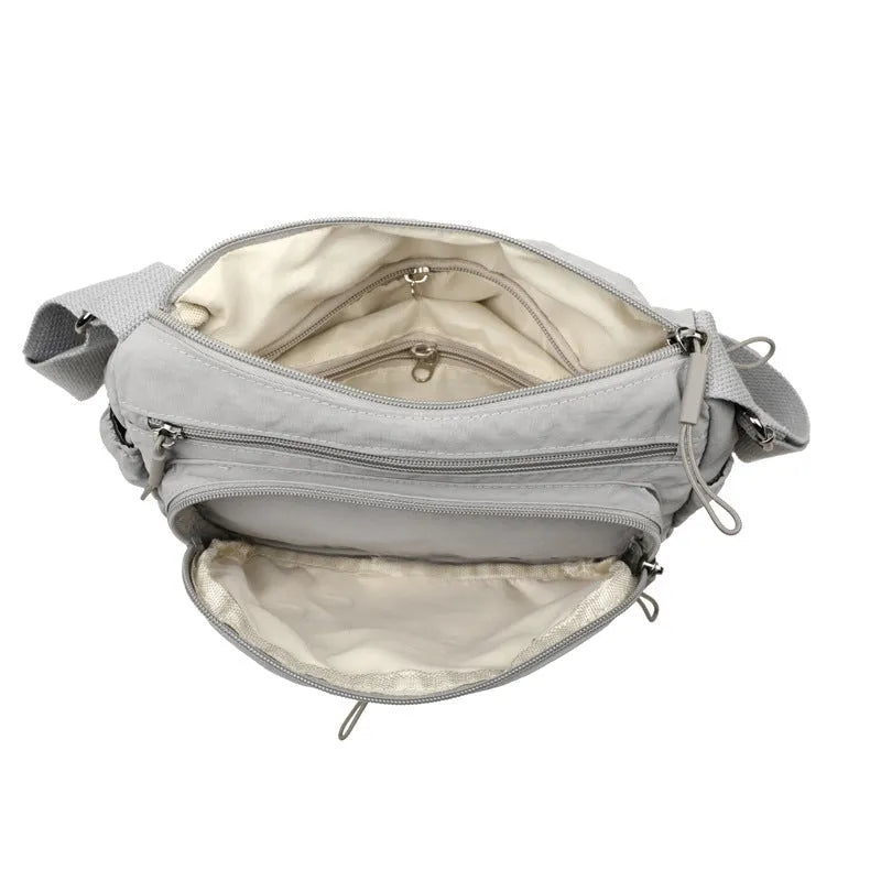 Soft water-repellent nylon crossbody bag in black, grey, or red, showing interior zipper pockets and an exterior 3D pocket.