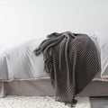 Small grey polyester nap blanket folded, showing its 127x170 cm size on a sofa.