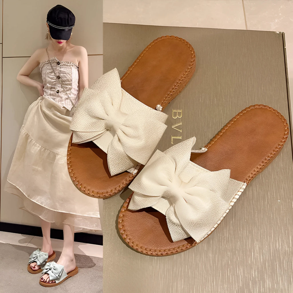 Women's beige slip-on sandals with a bow detail, suede cloth upper, and soft rubber flat sole.