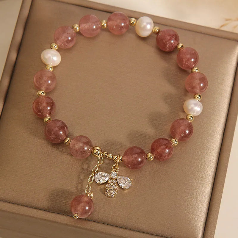 Close-up of a women's bracelet with strawberry quartz, freshwater pearls, a bee charm, and zircon accents on an alloy chain.