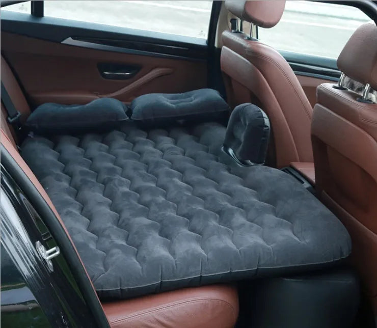 Inflatable car bed with flocking material shown in black colour, folded beside pillows and storage bag