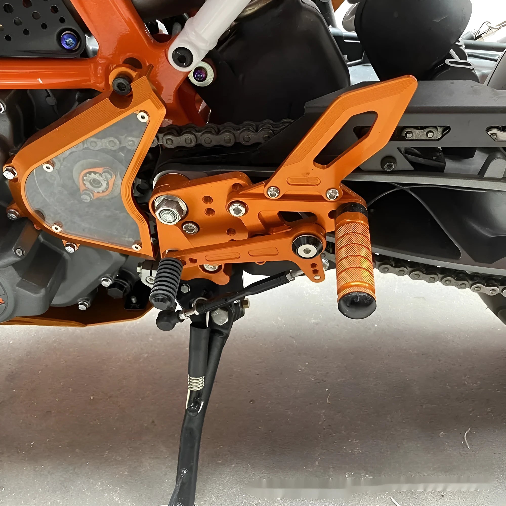 KTM Duke foot pedal bracket assembly for raised rear shift pedal in black or orange