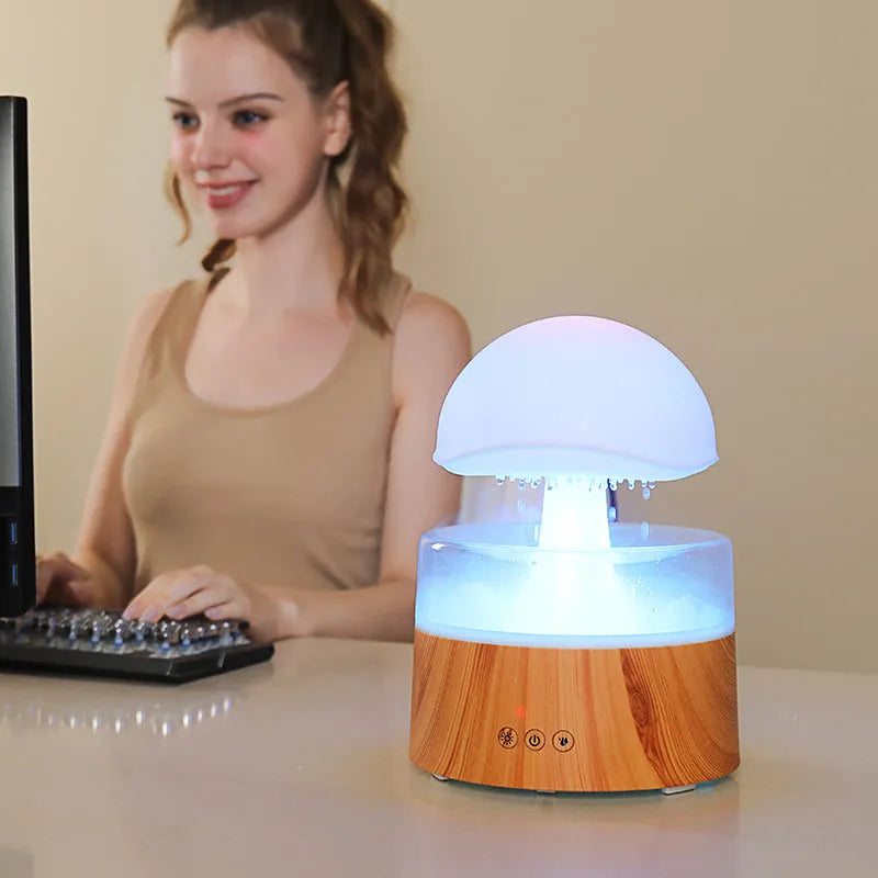 White cloud-shaped humidifier with simulated raindrops and colour-changing lights on wooden surface