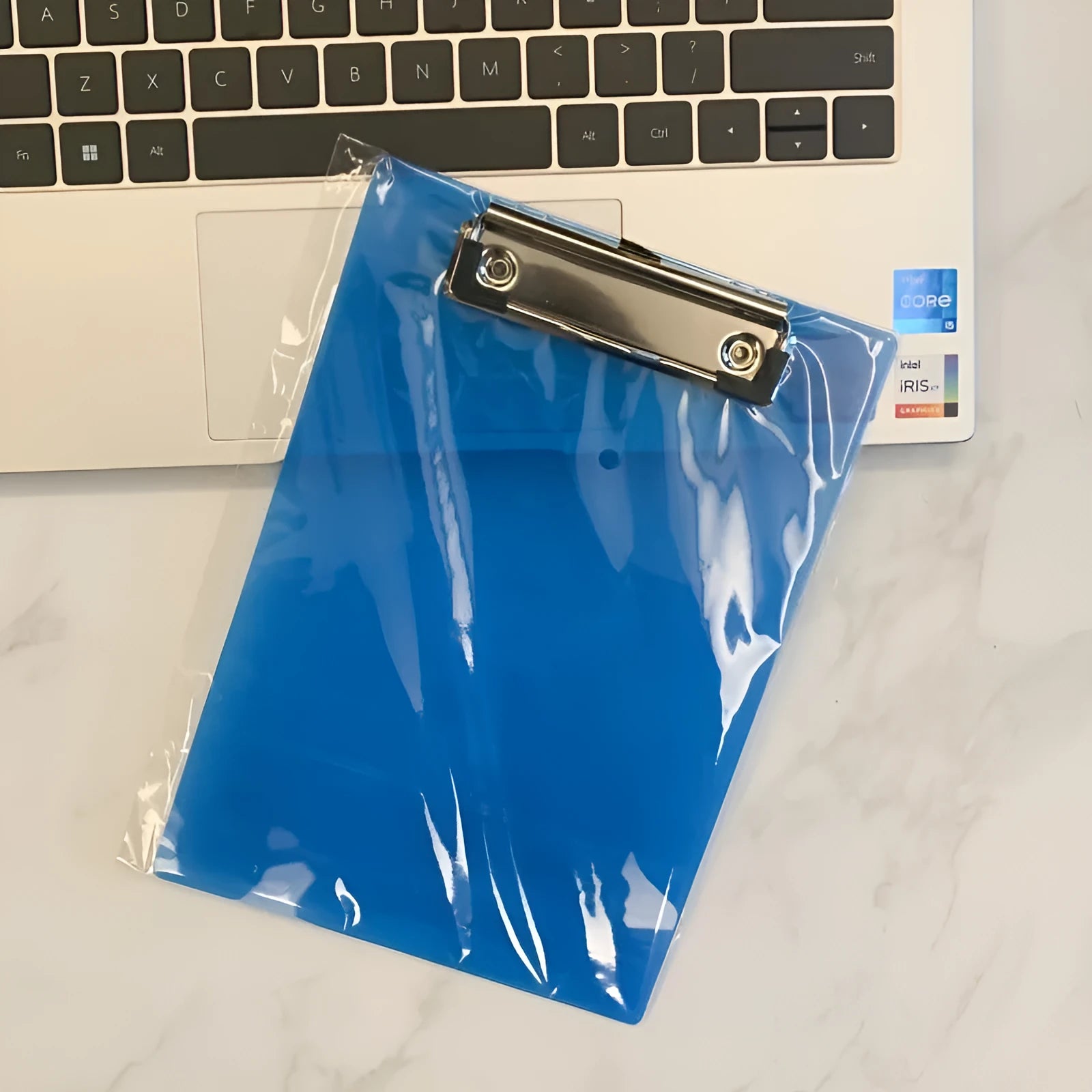 Transparent A4 clipboard with metal clip, shown in blue colour on a wooden desk.
