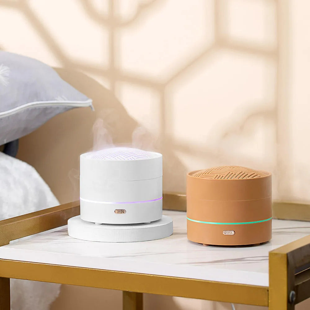 White ultrasonic aroma diffuser with four steam nozzles and LED light on a wooden table