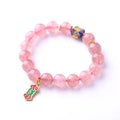 Close-up of a pink Strawberry Quartz crystal bracelet with hand-woven beads and a golden Ruyi symbol charm.