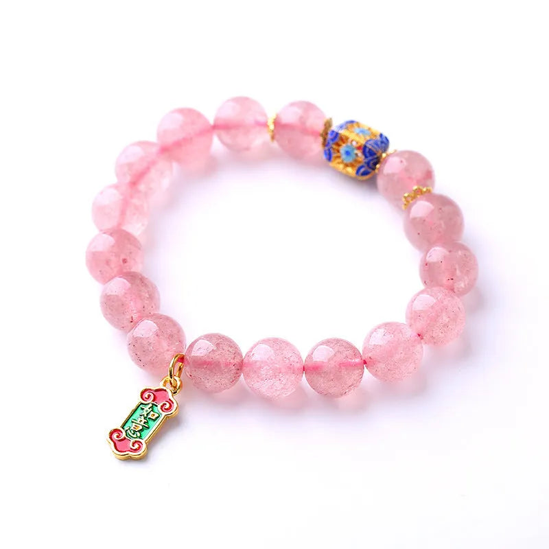 Close-up of a pink Strawberry Quartz crystal bracelet with hand-woven beads and a golden Ruyi symbol charm.
