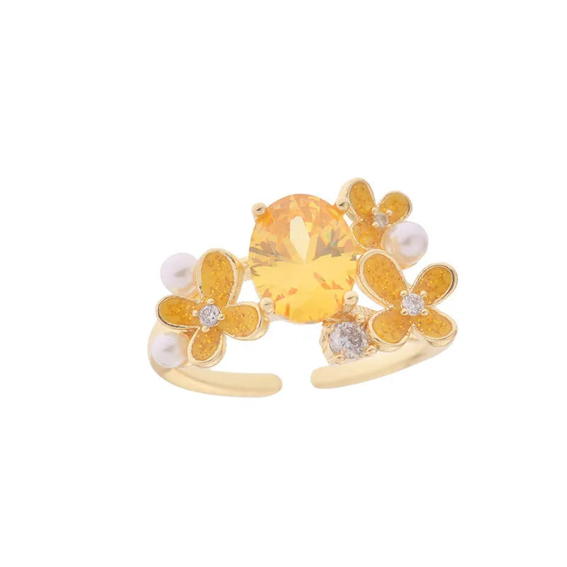 Yellow women's open ring with a flower shape and zircon detailing on a white background.