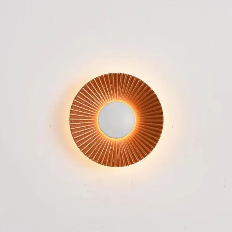 A round, modern wall lamp with an aluminium shade, shown in a two-tone gold and white finish, mounted on a wall.