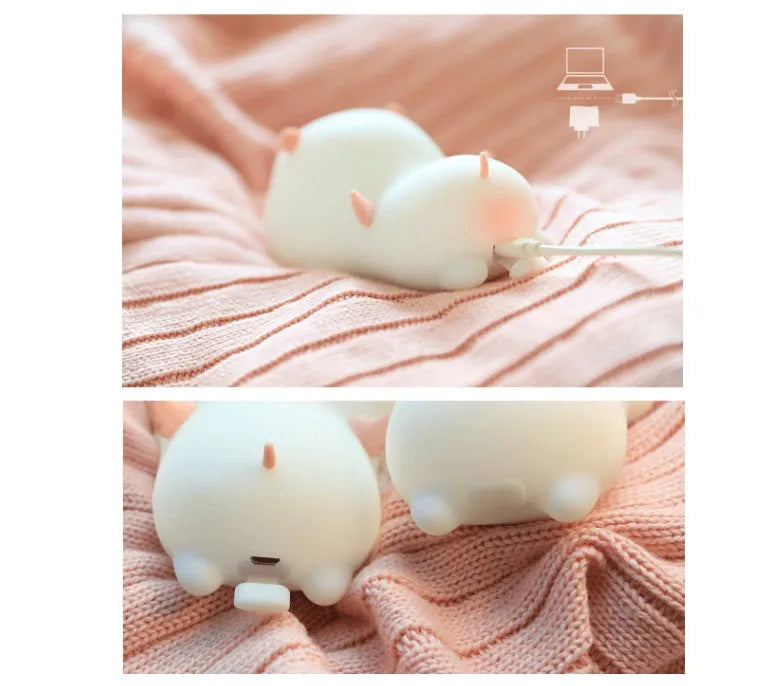 Blue rechargeable pig-shaped silicone night light with a sleeping design on a bedside table.