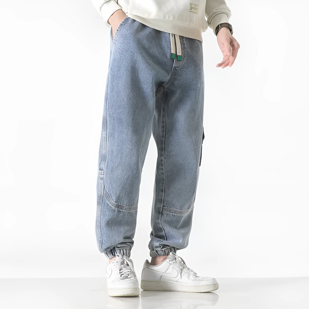 Man wearing loose-fit tapered trousers in grey, showing the mid-waist and tapered leg design.