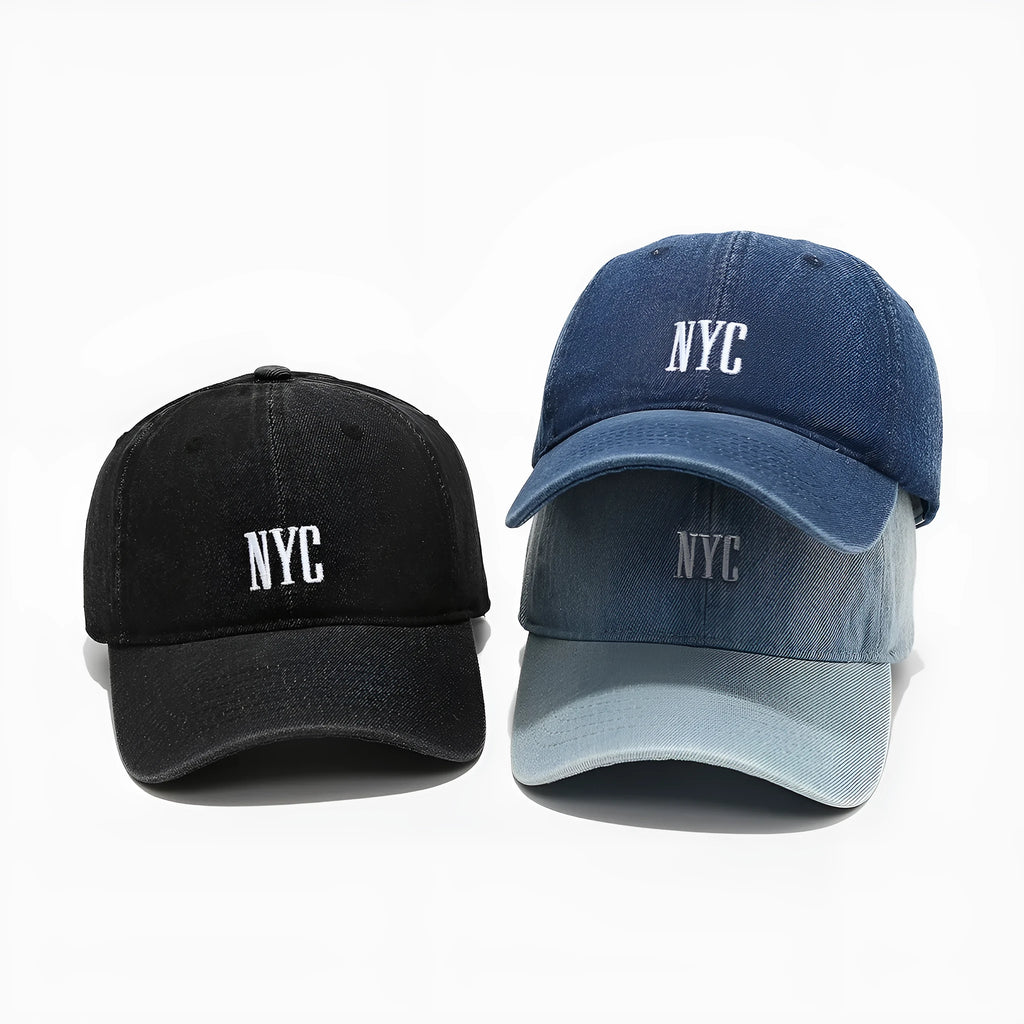 Light blue denim peaked cap with embroidered letters on a dome crown, showing adjustable strap.