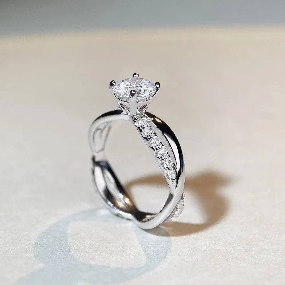 Close-up of a silver geometric ring with a twisted band and a 1-karat moissanite stone in a four-claw setting.
