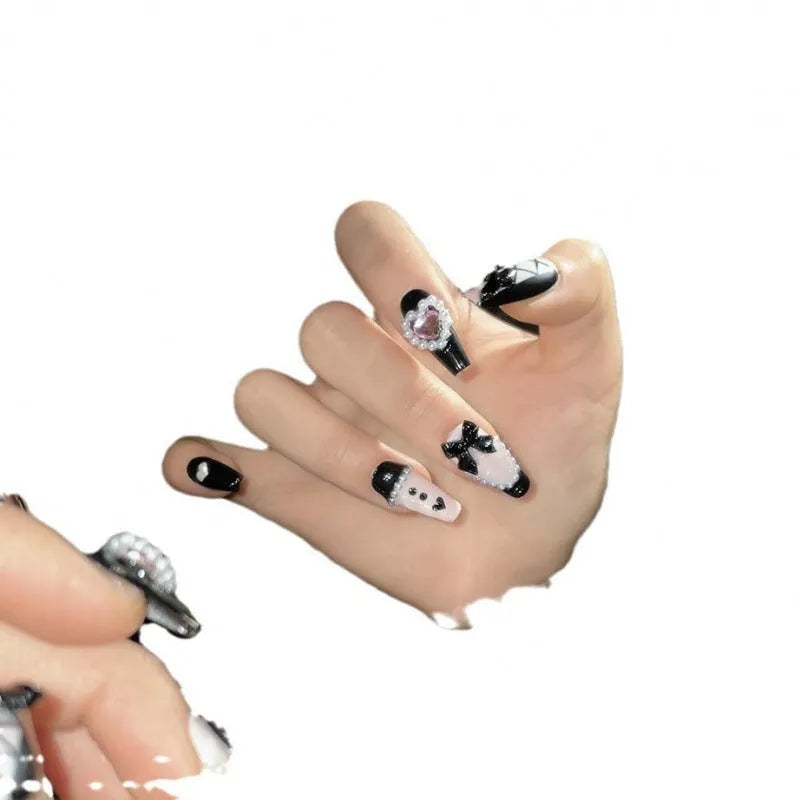 Black and pink heart-shaped hand-painted false nails with bow design, shown in mid-length cat's eye style.