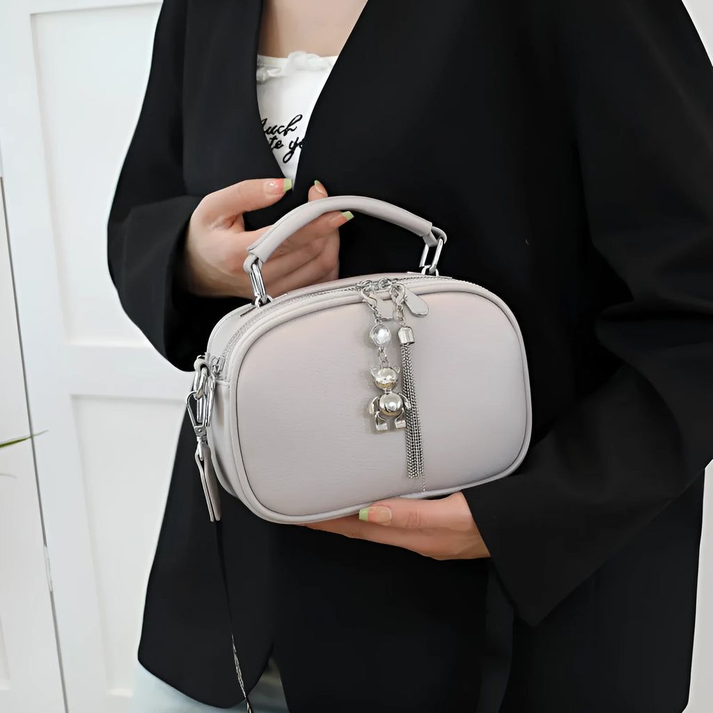 Women's small square stitching bag in oval shape with double shoulder strap showing internal mobile phone compartment.