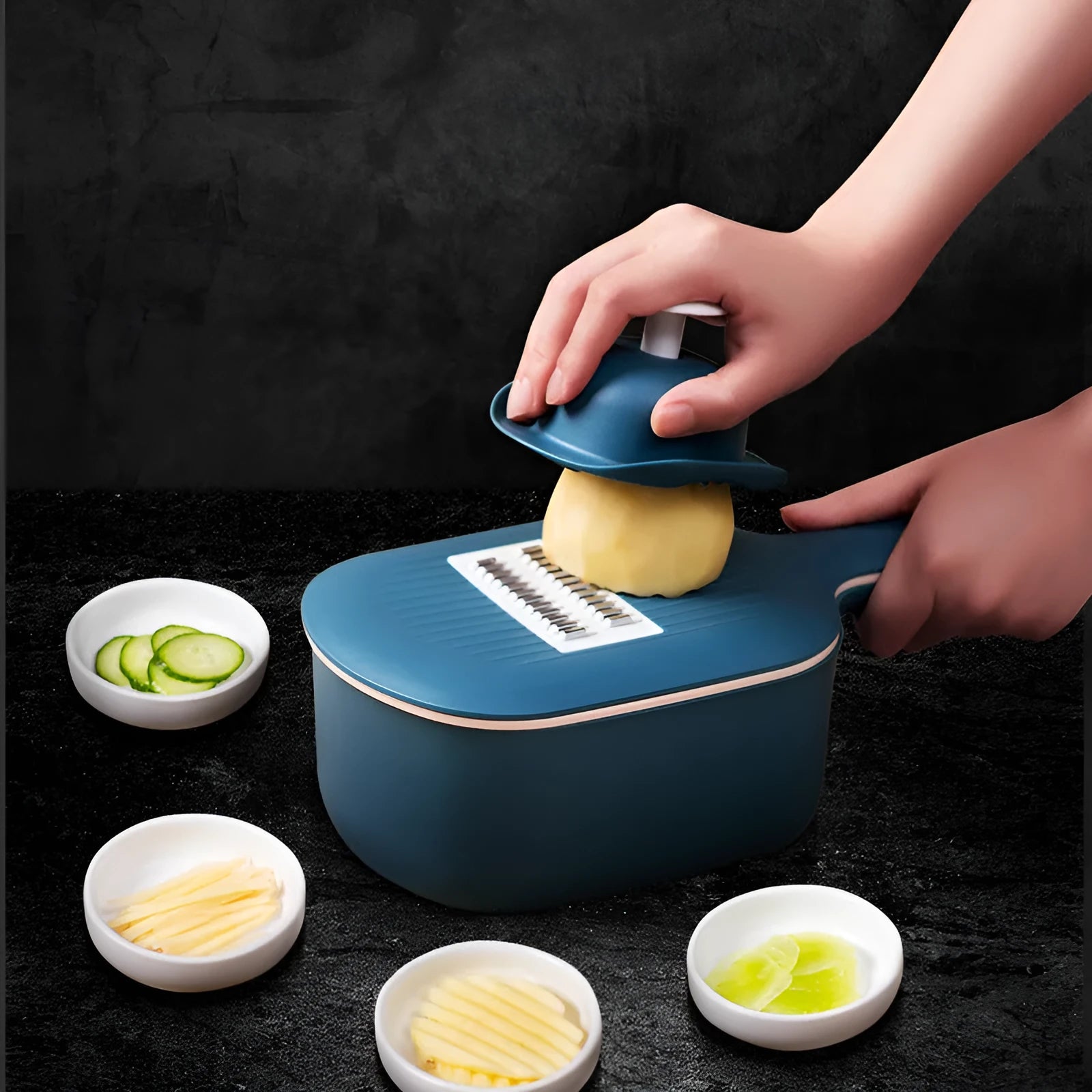 Dark blue manual vegetable cutter with four stainless steel blades, a hand protection guard, and a drain basket on a kitchen counter.