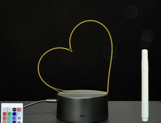 Black 3D acrylic message board lamp with remote control and marker pen on a desk.