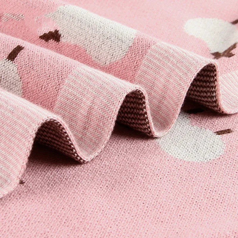 Grey and pink baby sheepskin blanket measuring 100cm by 80cm on a crib