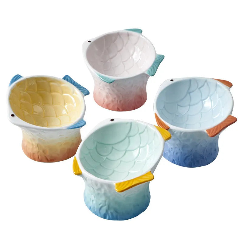Set of four blue fish-shaped ceramic cat bowls on a table, showing elevated shallow design and tilt angle.