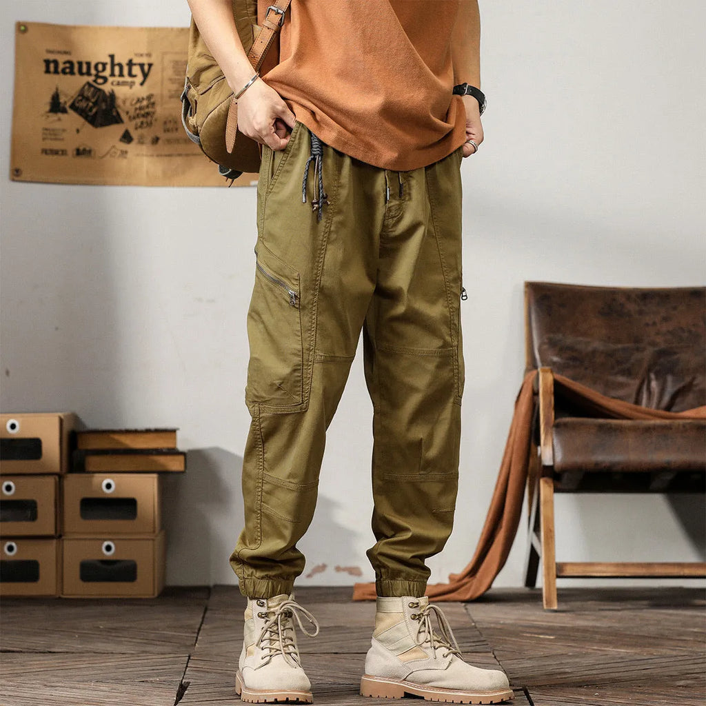 Men's khaki cotton harem pants with tapered ankle cuffs and a loose fit, shown laid flat.