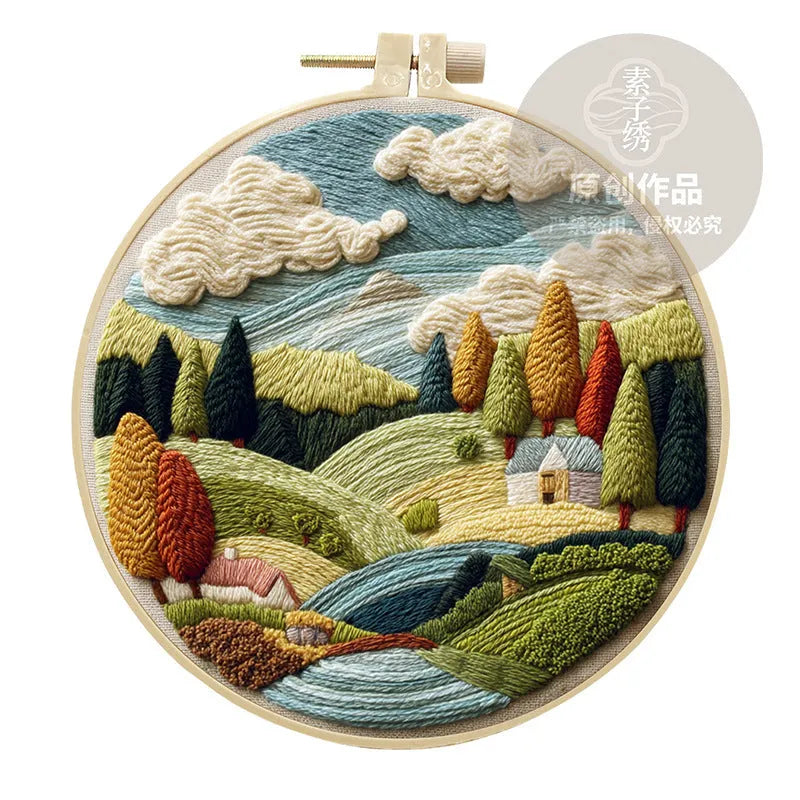 DIY embroidery kit components: printed cotton landscape fabric, embroidery threads, needles, and a bamboo hoop.