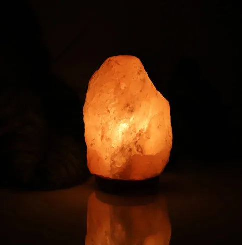 Rose crystal salt lamp with natural rock salt shade on a bedside table, warm glow, compact size.