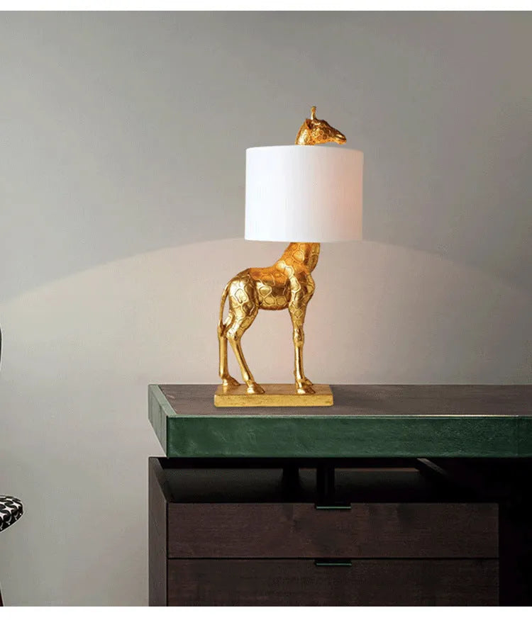 A tall white giraffe table lamp with a cloth shade on a wooden desk.