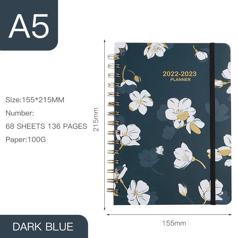 A5 spiral-bound notebook with a colourful floral design cover, lying open on a table.