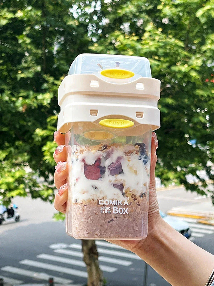 A portable bento box with two compartments for storing different types of food, such as salad, yogurt, oatmeal, and milkshake.