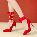 Black pointed toe stiletto shoe with a lace ankle strap and flat buckle on a 12cm heel.