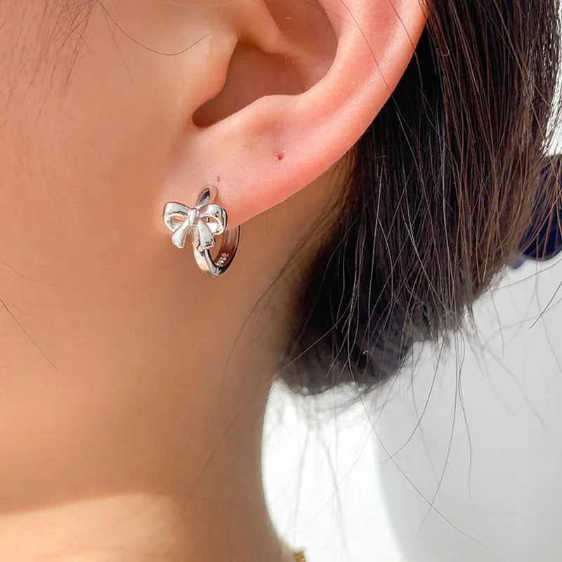 A pair of 925 sterling silver bow earrings in silver colour with electroplating finish on a plain background