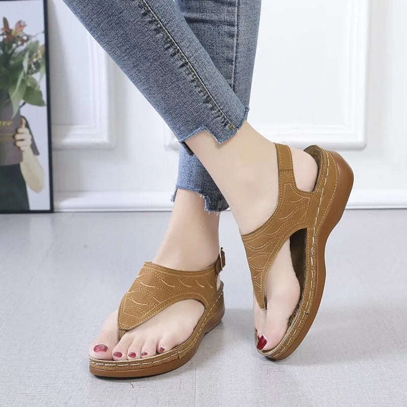 Women's beige wedge heel flip flop sandals with an adjustable buckle strap on a wooden deck.