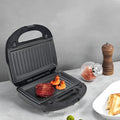 Black double-sided electric sandwich pan with brushed stainless steel lid on kitchen counter