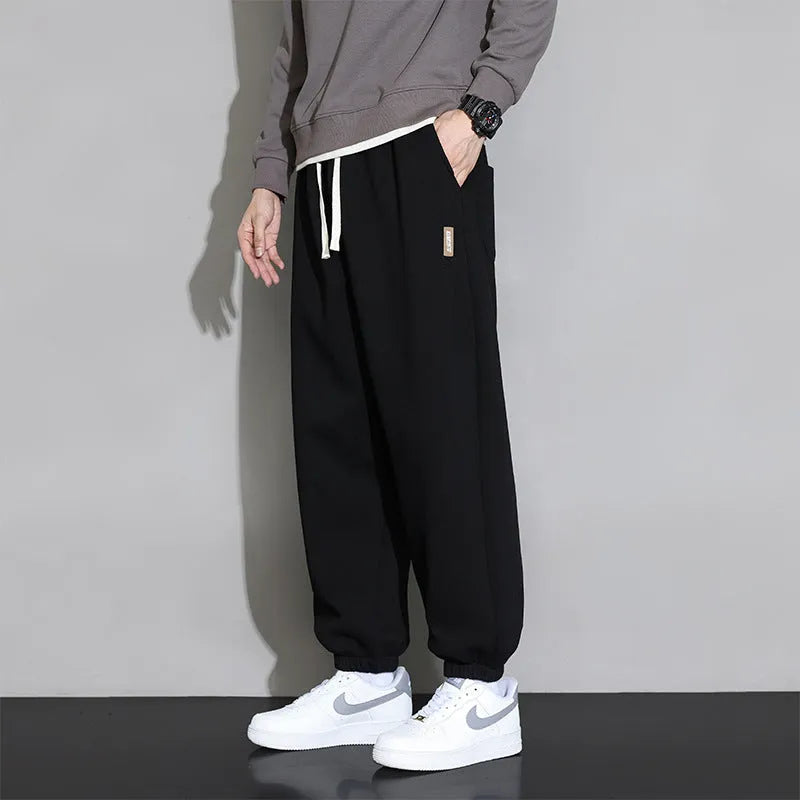 Men's loose grey cotton blend sports trousers with drawstring waist on a hanger.