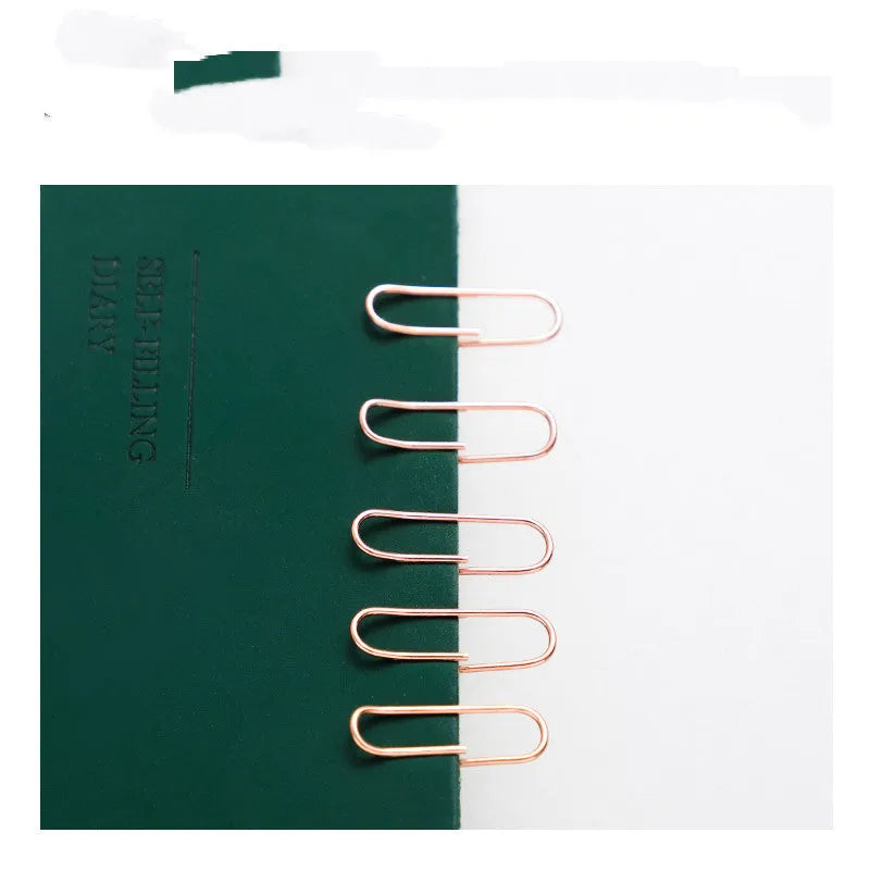 Box of 100 small rose gold heart-shaped metal paper clips on a white surface.