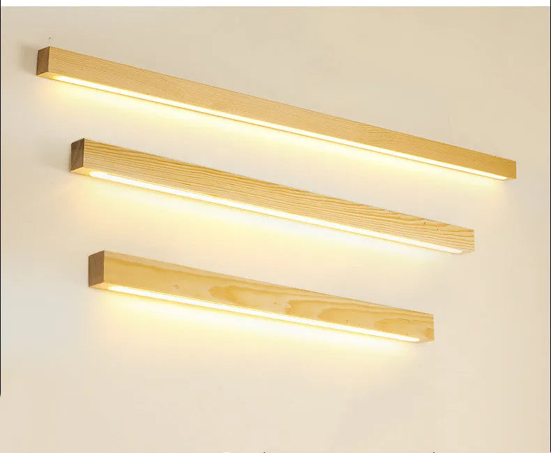Long, slim walnut-coloured wooden wall lamp with integrated LED lighting on a plain wall.