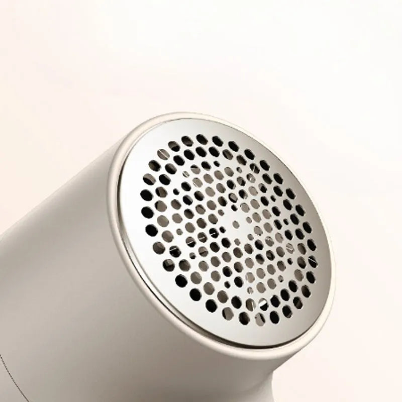 White electric lint remover with LED display, USB port, and stainless steel cutter head on a fabric background.