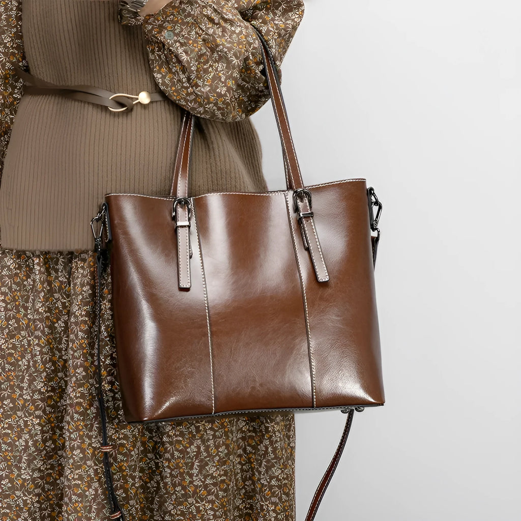Brown genuine leather retro women's shoulder tote bag with three straps on a table.