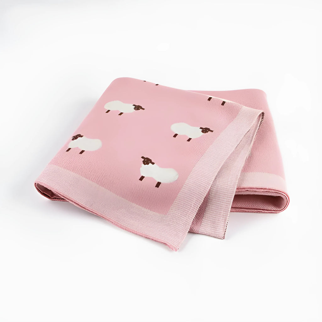 Grey and pink baby sheepskin blanket measuring 100cm by 80cm on a crib