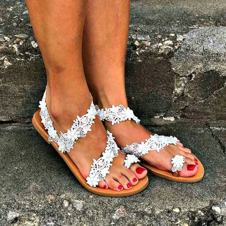 White women's slip-on flat shoes with floral and rhinestone decoration on the upper.