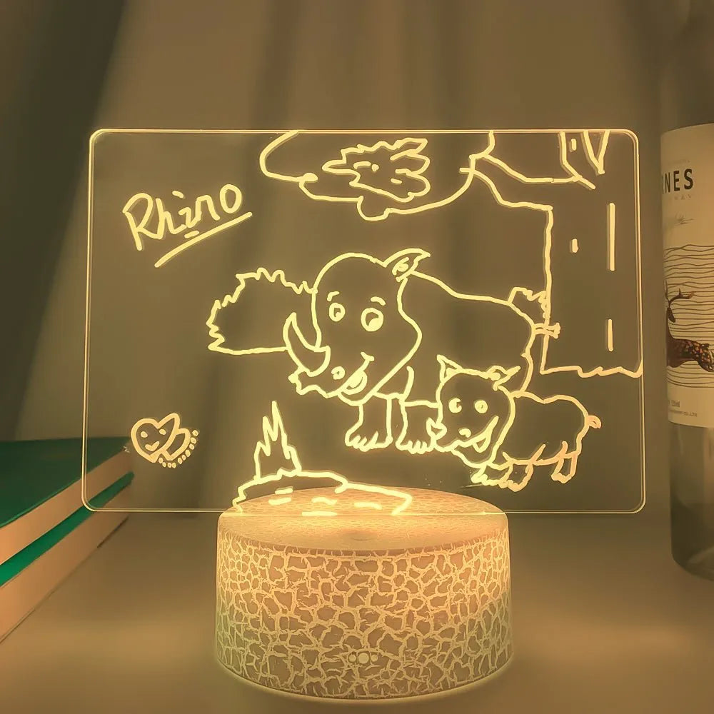 Black 3D acrylic message board lamp with remote control and marker pen on a desk.