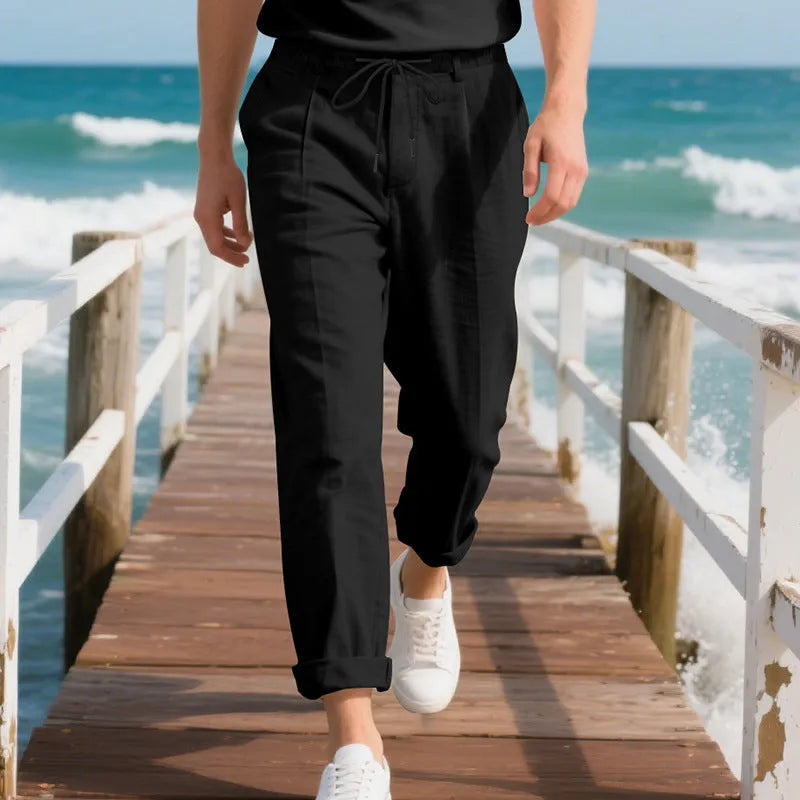 Men's light beige linen trousers with drawstring waist and straight-leg design laid flat